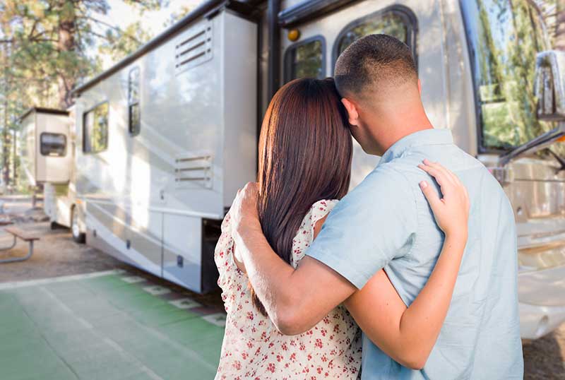 Young couple hugging in front of their new motorhome after rv inspection services are scheduled